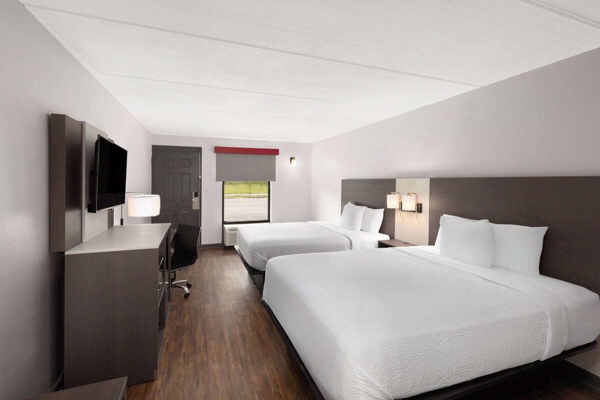 Quarto de hotel com duas camas, uma escrivaninha, televisão e janela com vista.