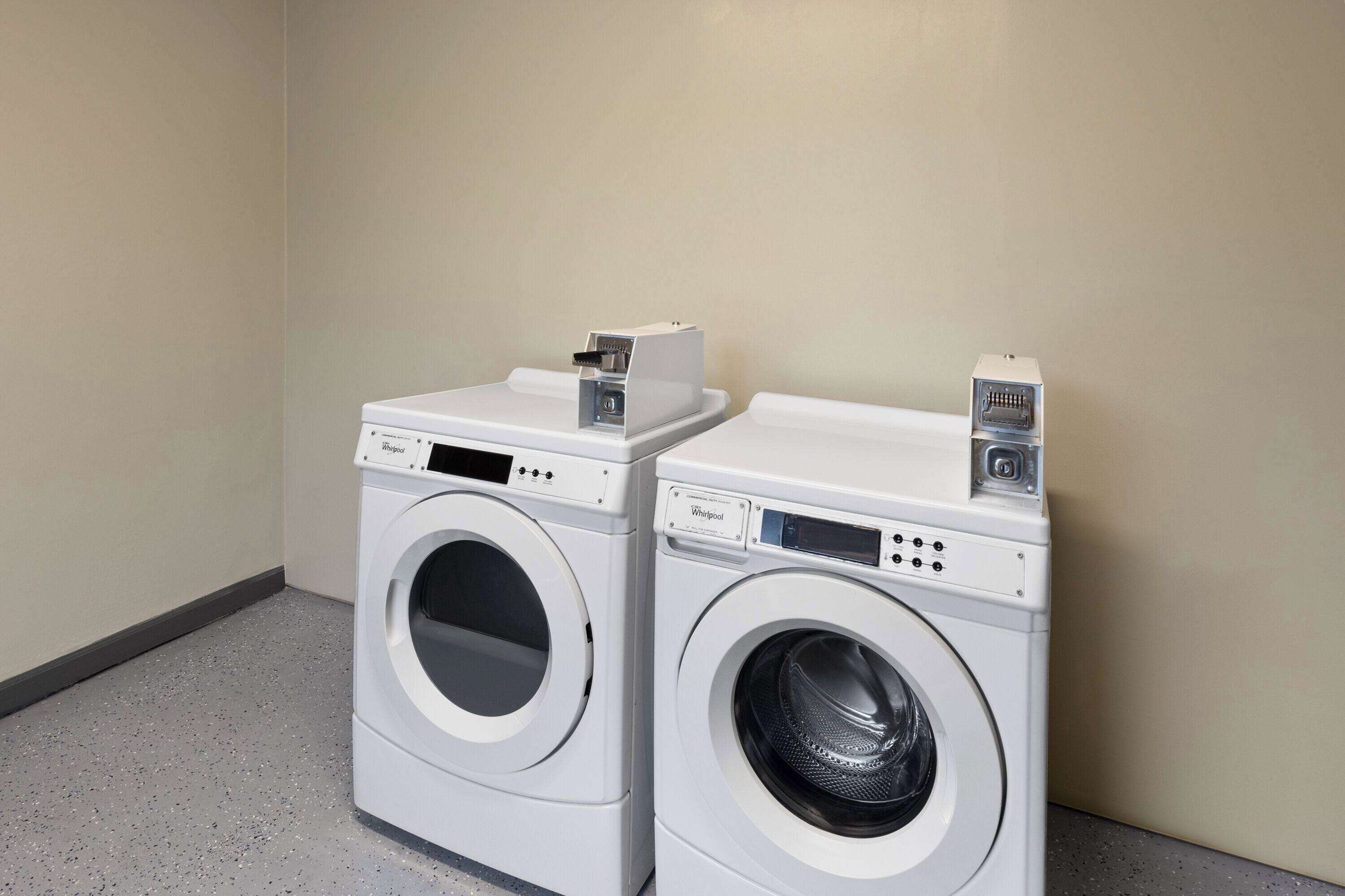 Deux machines à laver à chargement frontal sont placées dans un coin, contre un mur uni et au-dessus d’un sol à motifs.