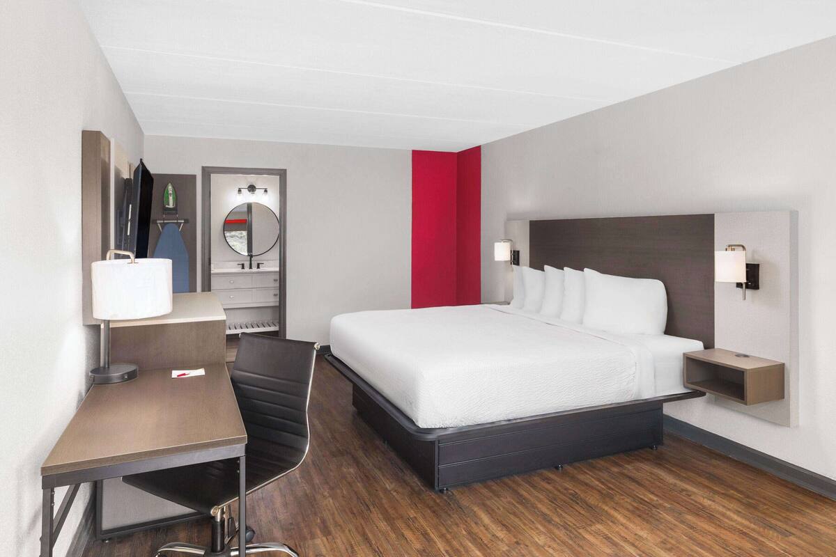 Quarto de hotel com cama, escrivaninha, cadeira e espelho.