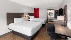 A hotel room with two beds, a desk, a chair, a TV, a mirror, and a red accent wall. - Ramada by Wyndham Bainbridge (Bainbridge)