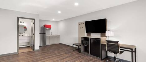 A modern hotel room with a wooden floor, a desk with a chair, a flat-screen TV, a microwave, and a refrigerator.