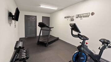 A fitness room with a treadmill, stationary bike, and weight bench.