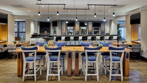 A modern dining area with multiple tables and chairs, a bar in the background, and a large TV on the wall. - Detroit Metro Airport Marriott (Romulus)