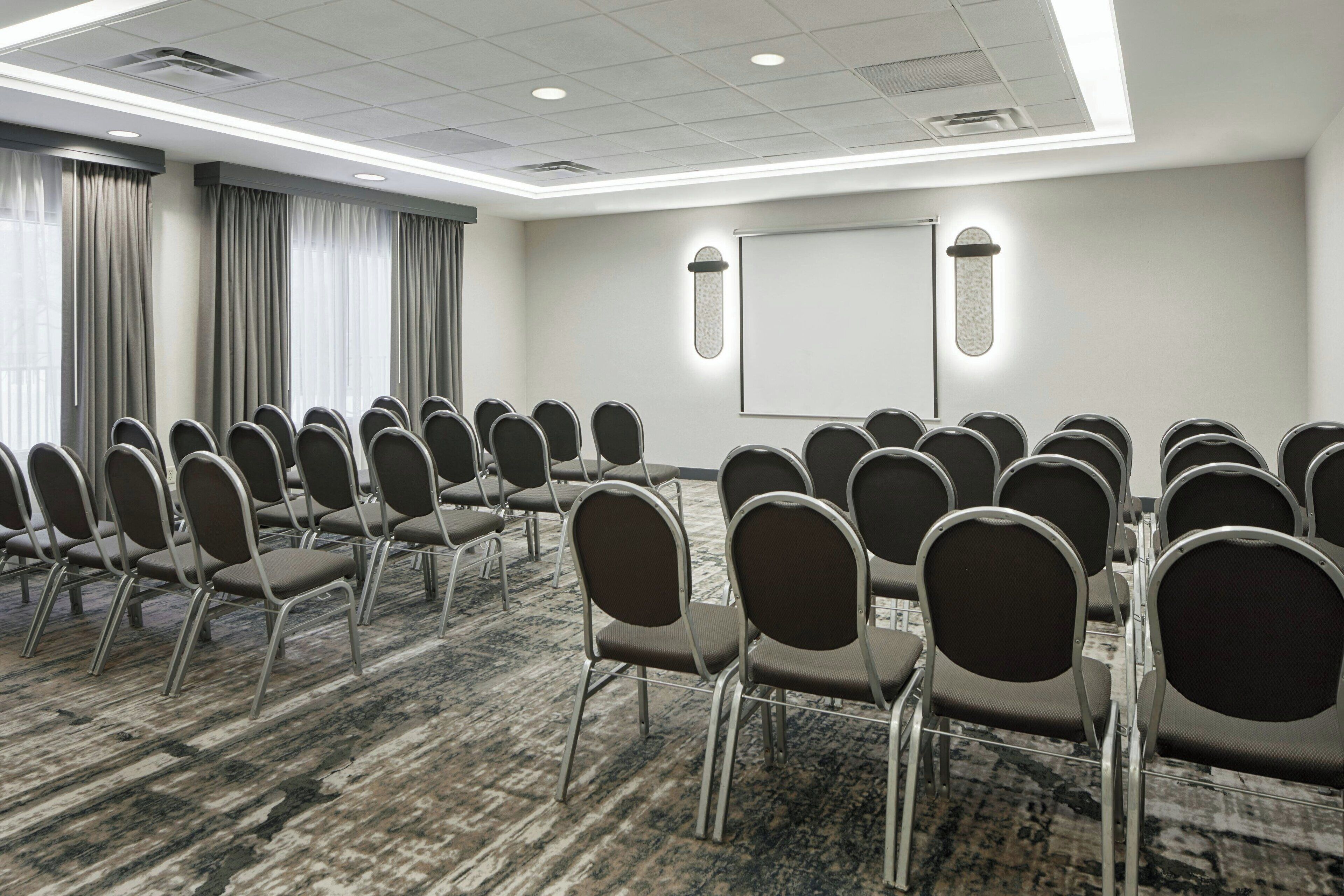 A conference room with rows of chairs, a projector screen, and a carpeted floor.