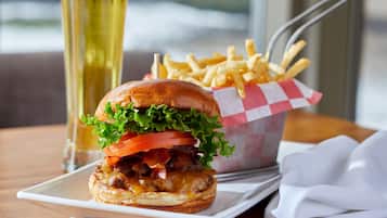 A burger with lettuce, tomato, and bacon, a glass of beer, and a basket of fries on a table.