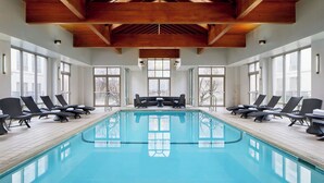 A large indoor swimming pool with wooden beams, sunlit windows, and lounge chairs. - Detroit Metro Airport Marriott (Romulus)
