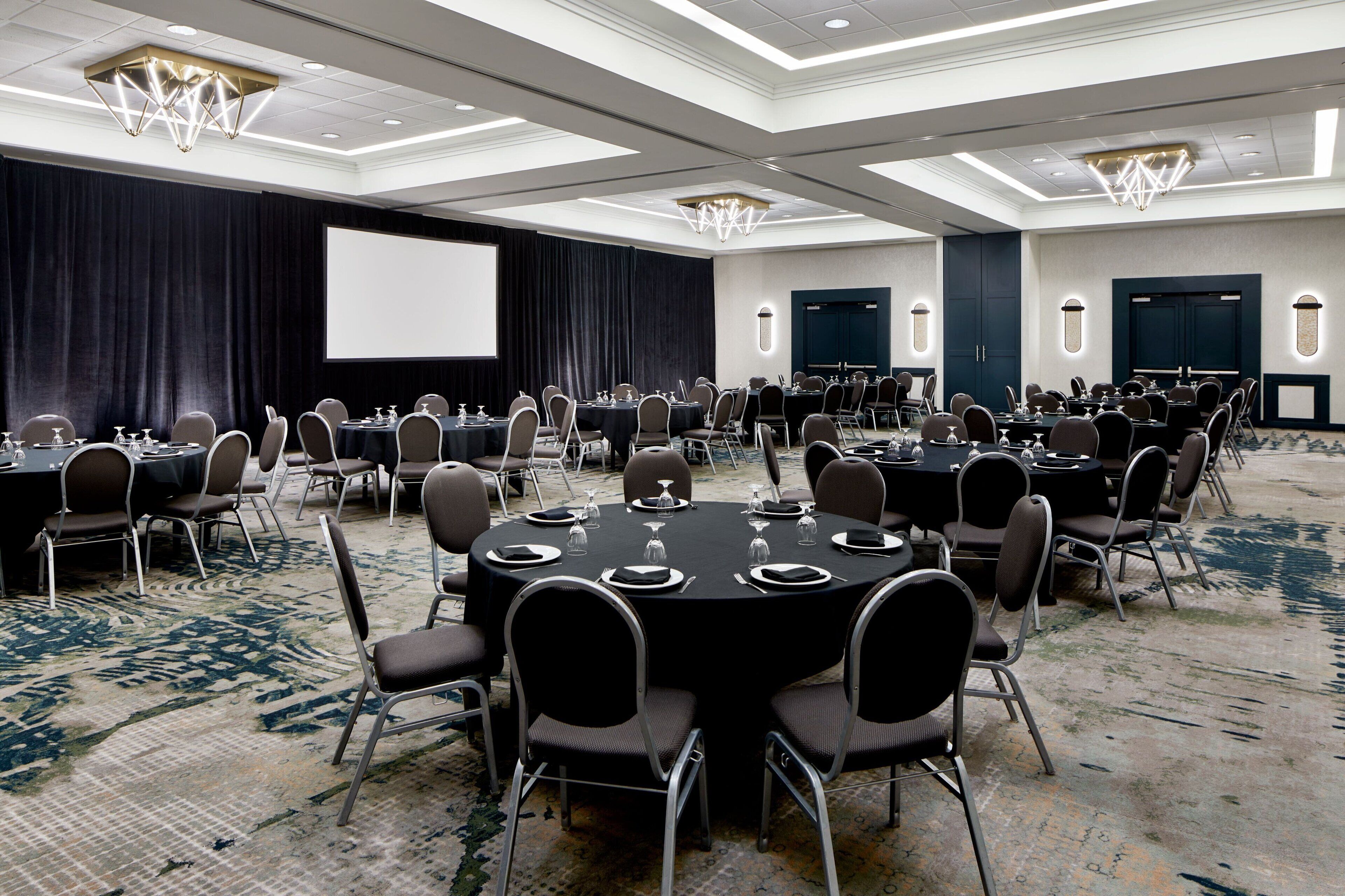 A conference room with round tables, chairs, and a large screen.