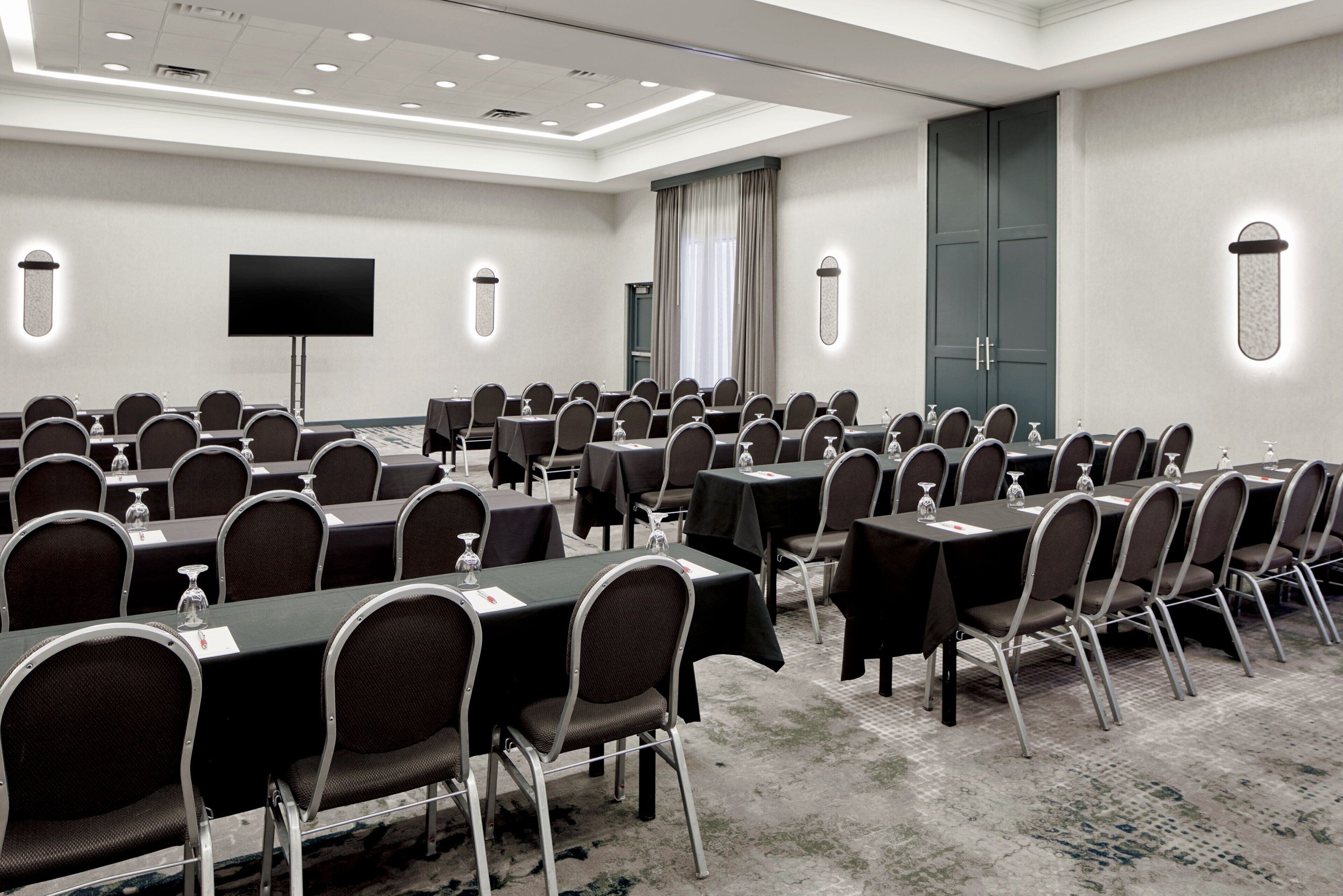 A conference room with multiple tables and chairs, a flat-screen TV, and a large door.