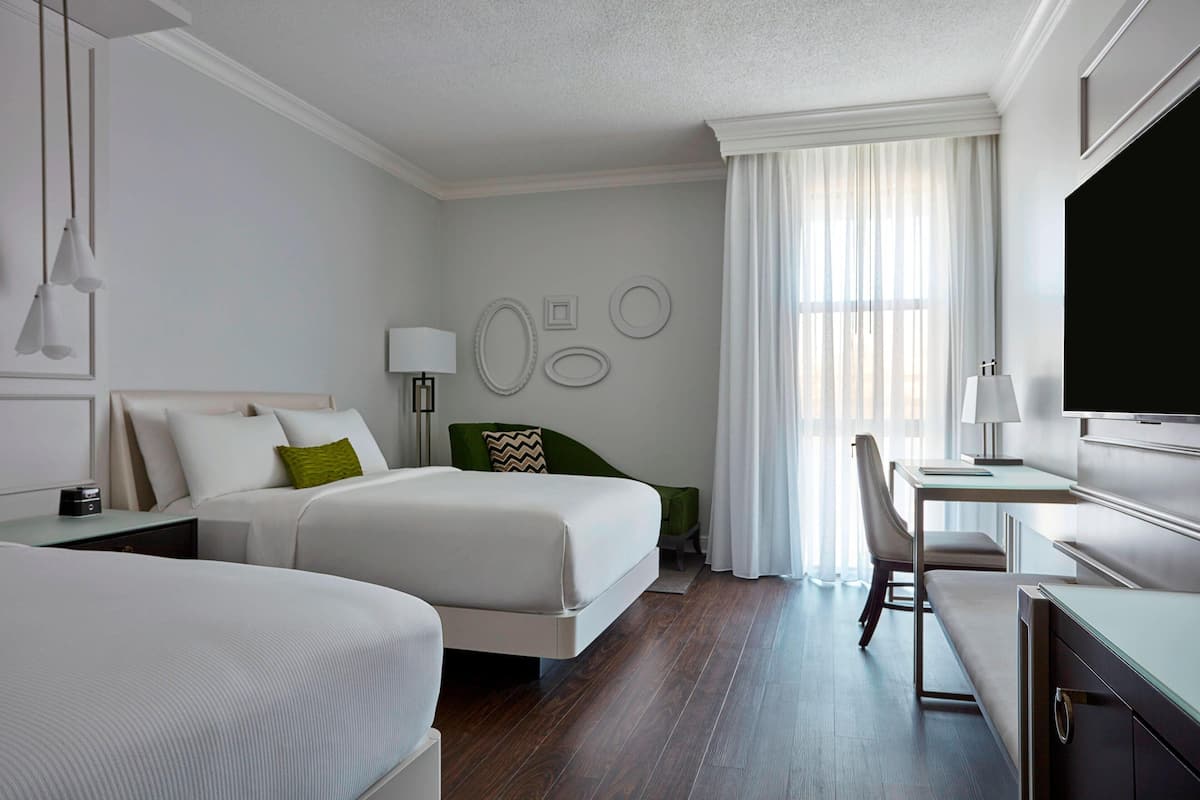 A modern hotel room with two beds, a desk, and a TV.