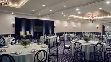 A banquet hall with round tables, black chairs, and chandeliers.