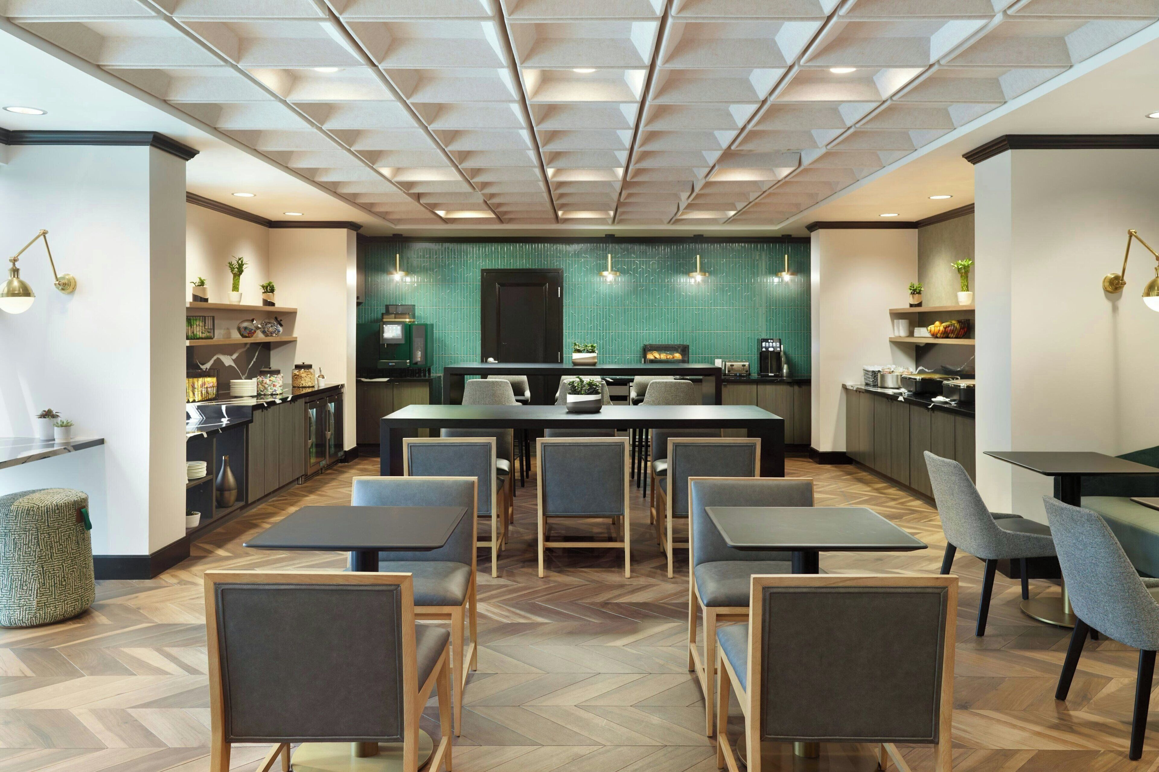Un espace de salle à manger moderne avec une table centrale, des chaises disposées autour, et une cuisine en arrière-plan.