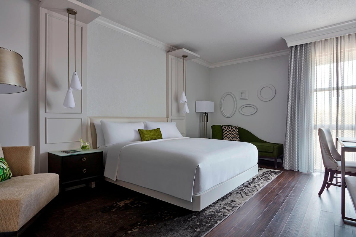 A hotel room with a large bed, a desk with a chair, a nightstand, and a lamp.