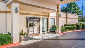 A hotel entrance with a glass door, a number '2945' above the door, a bench, and potted plants. - Quality Inn Suwanee I-85 (Suwanee)