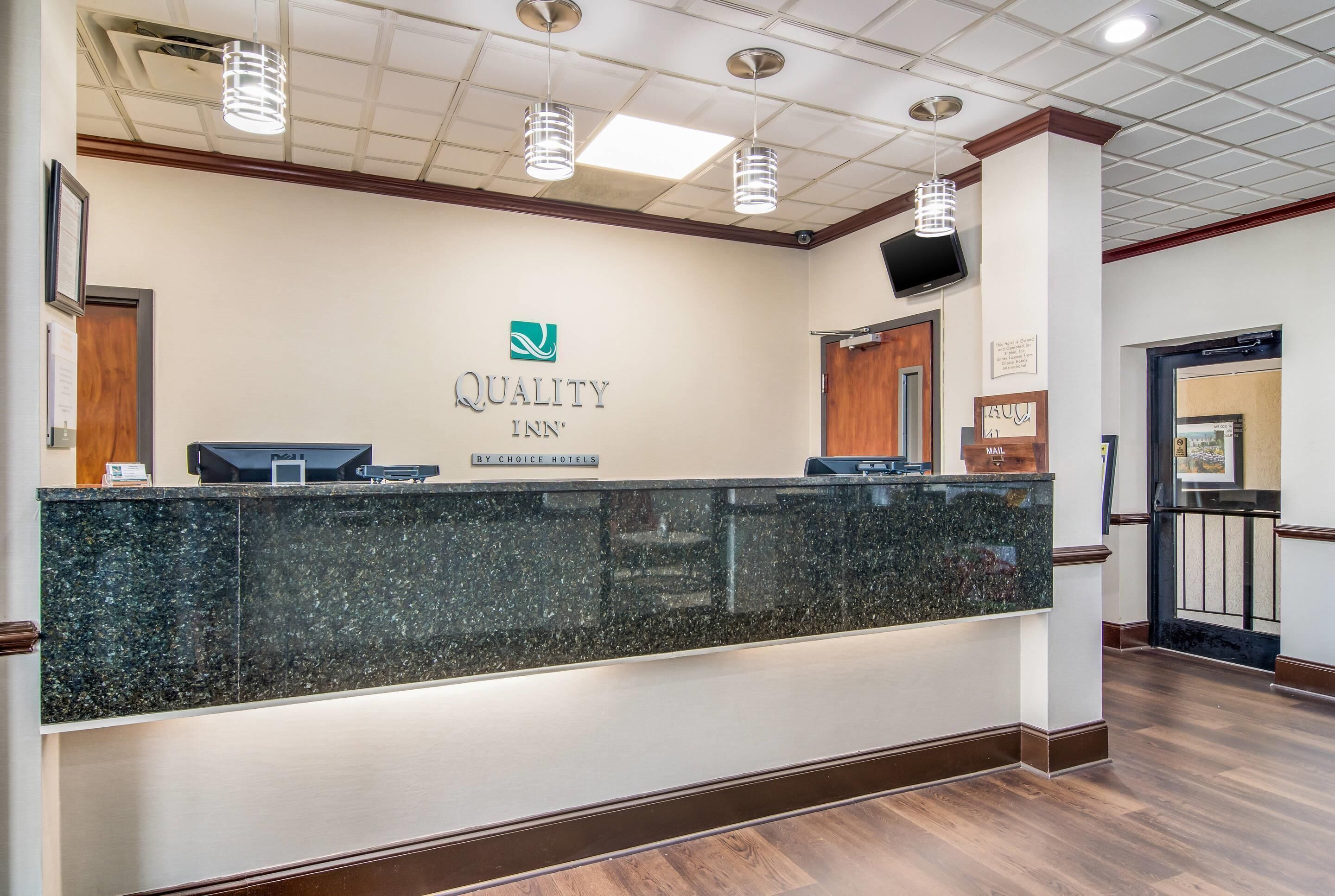 A hotel reception desk with a logo, a digital screen, and a sign indicating it's a Quality Inn by Choice Hotels.