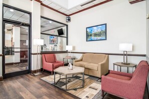 A hotel lobby with a sofa, armchairs, a coffee table, a TV, and a framed picture on the wall.