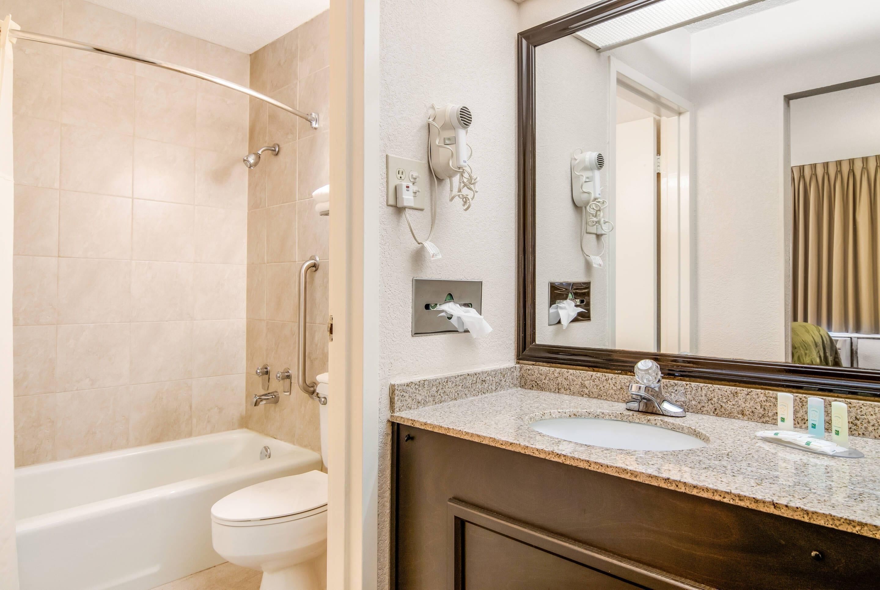 Un baño con bañera, inodoro, lavabo y secador de pelo montado en la pared.