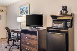 Habitación de hotel con escritorio, silla, televisión, microondas y cafetera.