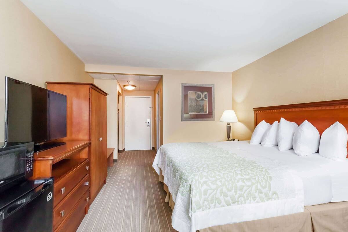 A hotel room with a bed, a TV, a dresser, and a door leading to another room.