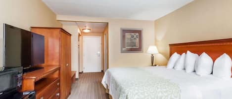 A hotel room with a bed, a TV, a dresser, and a door leading to another room.