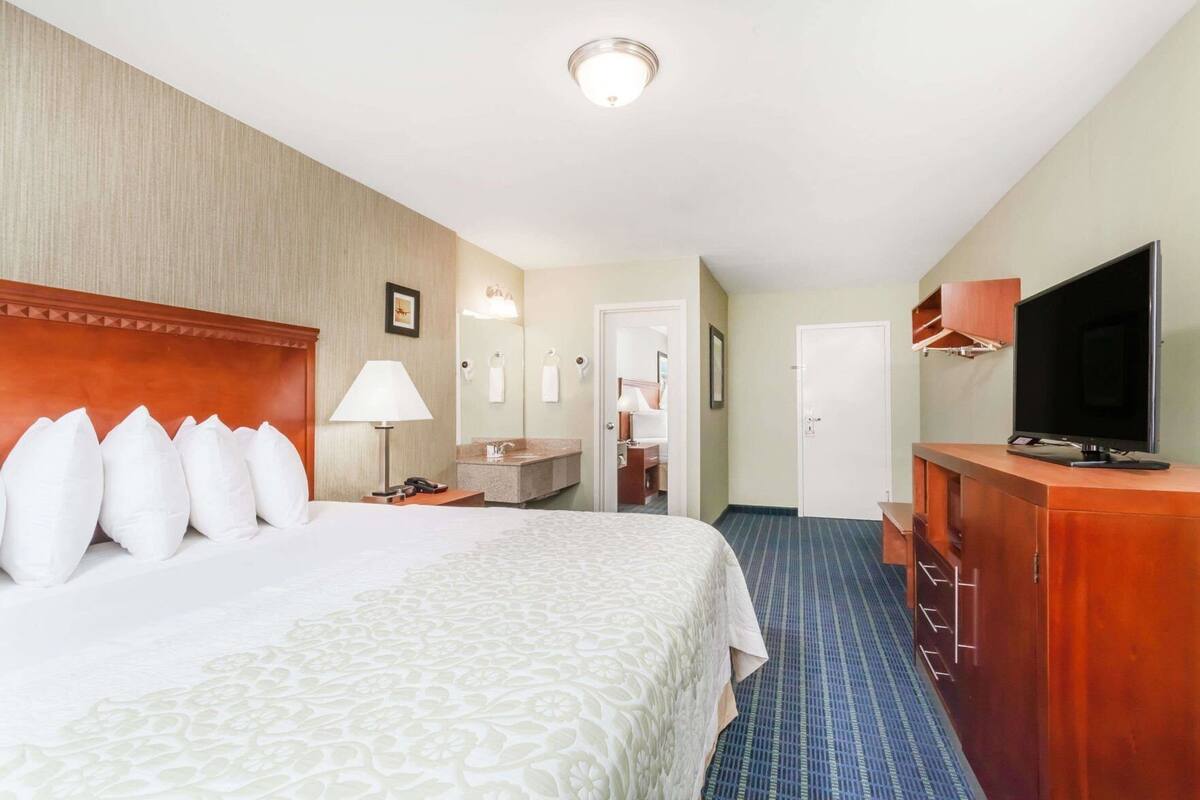 A hotel room with a bed, a desk, a television, and a bathroom visible through an open door.