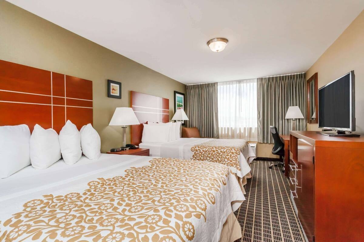 A hotel room with two beds, a desk, a TV, and a window with curtains.