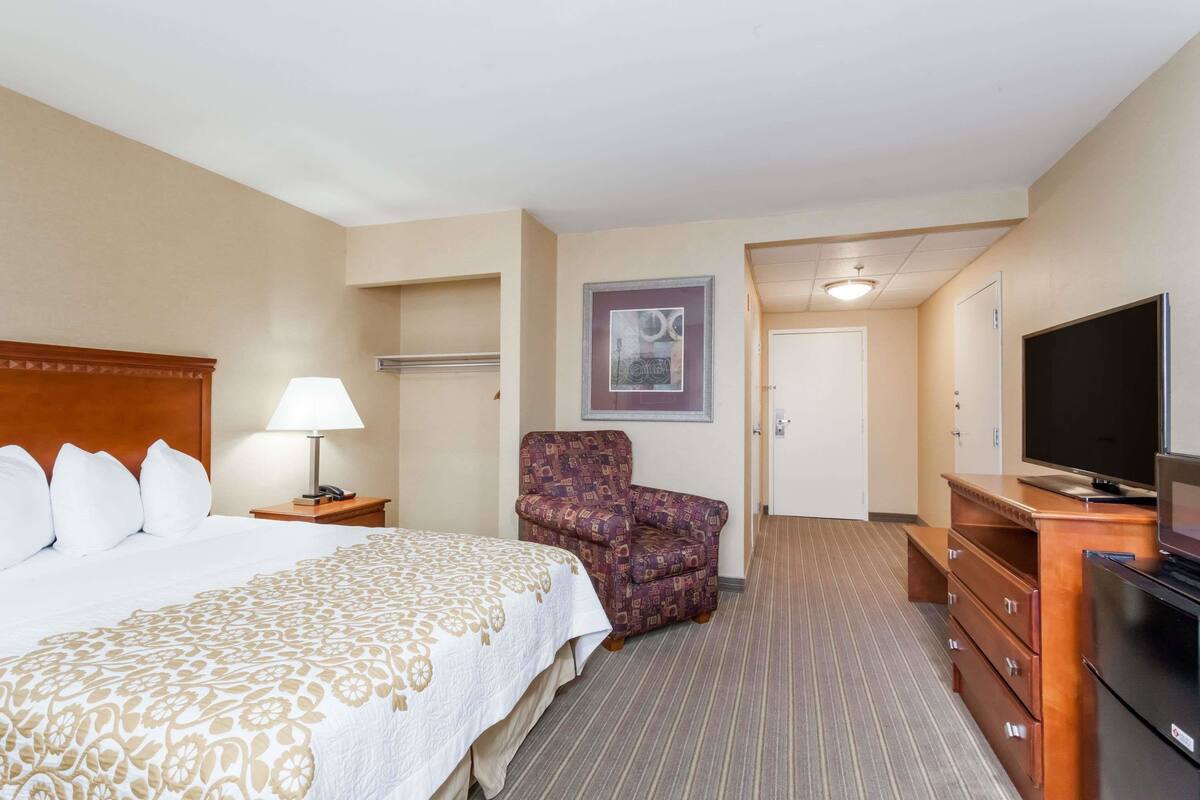 A hotel room with a large bed, a chair, a TV, and a dresser.
