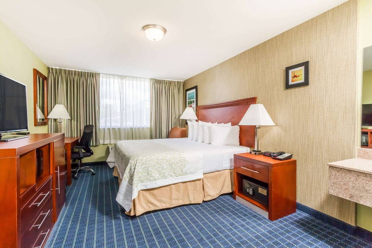 A hotel room with a large bed, a desk with a TV, a chair, a desk lamp, a bedside table with a phone, and a small bathroom area.