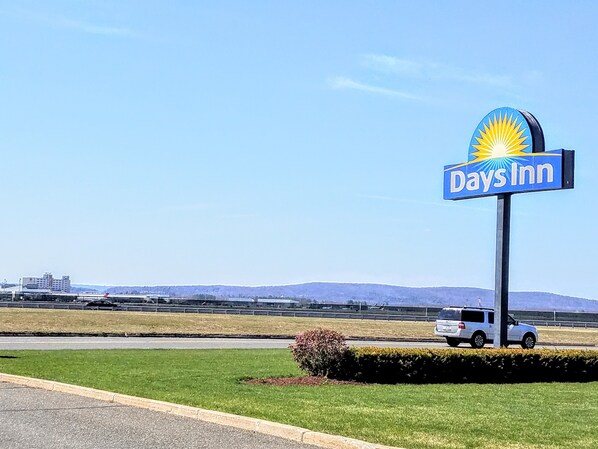 A Days Inn sign with a sun logo, located near a road with a grassy area and a distant mountain range. - Days Inn by Wyndham Windsor Locks / Bradley Intl Airport (Windsor Locks)