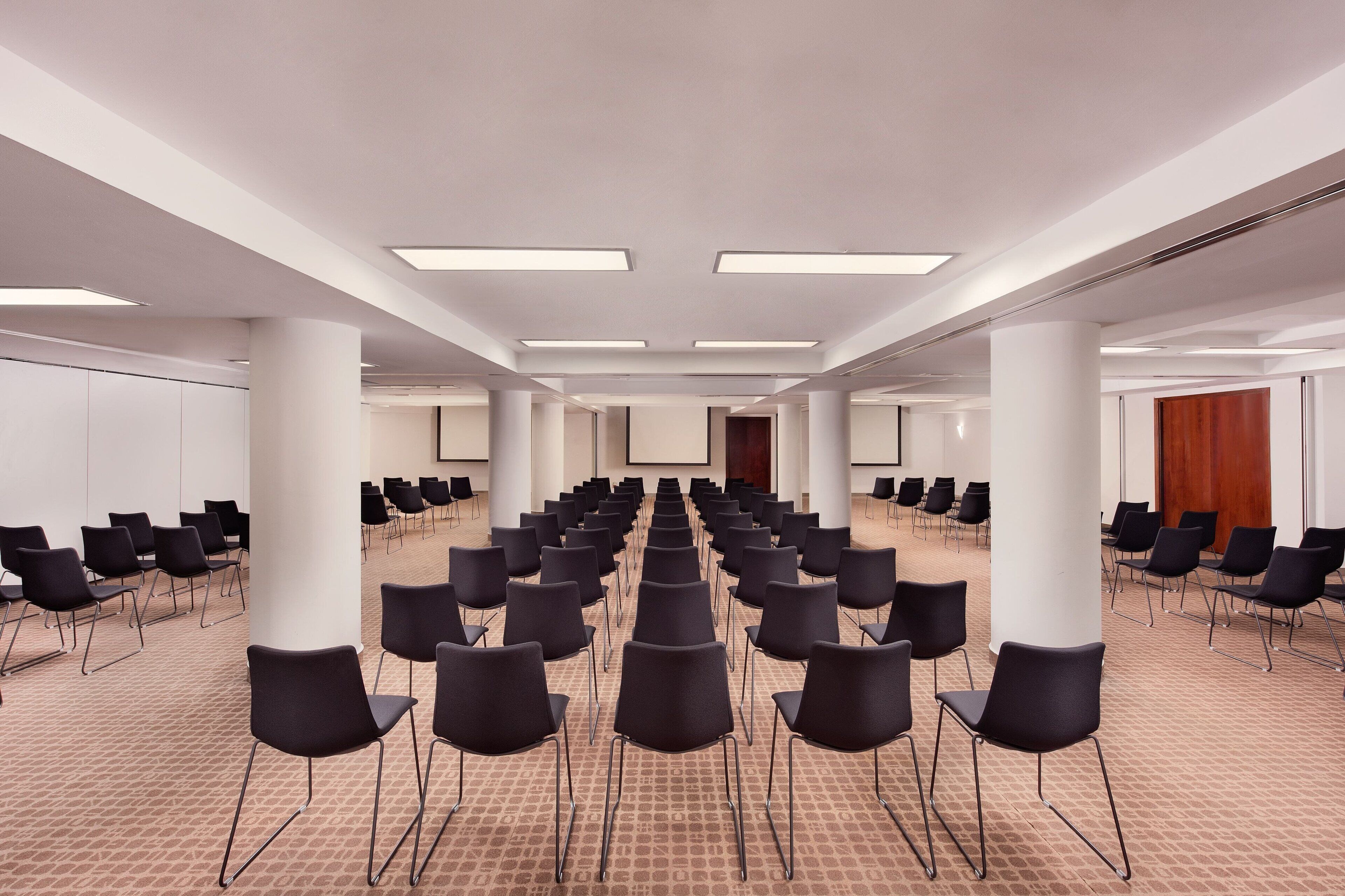 Ein Konferenzraum mit Reihen schwarzer Stühle, weißen Säulen und einem Teppichboden.