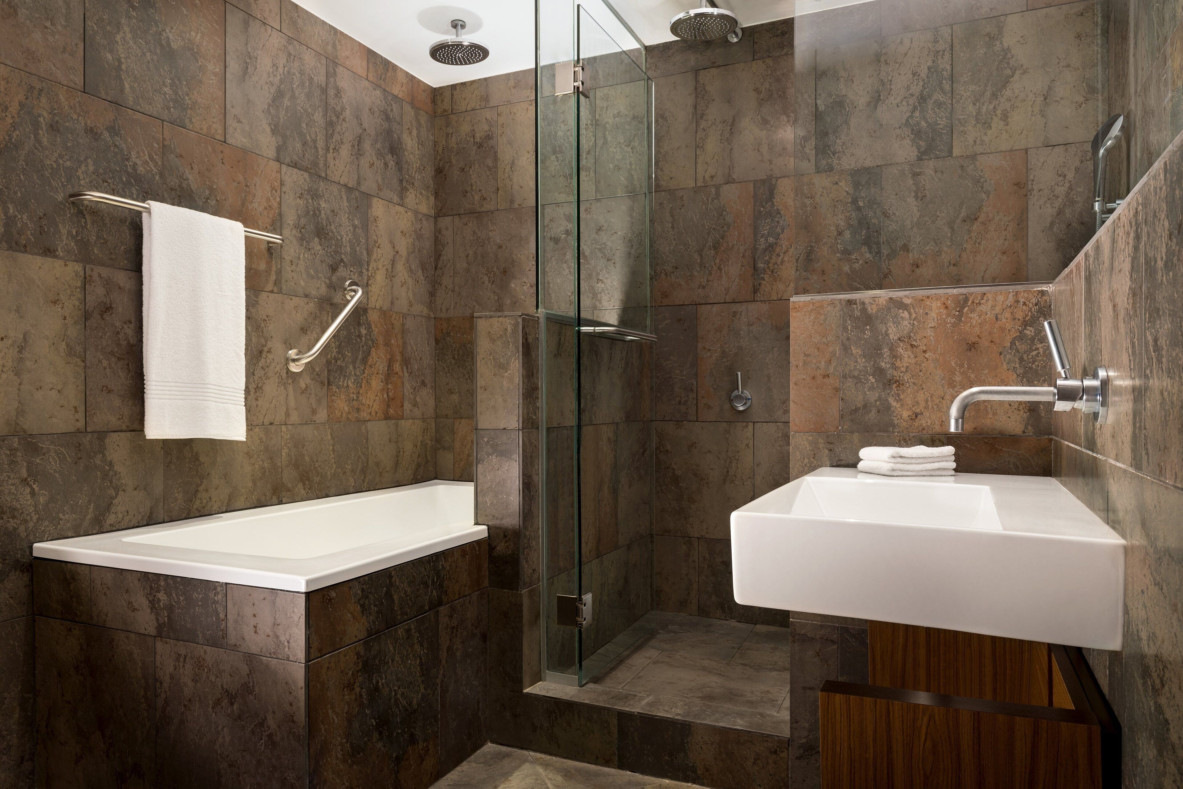 A modern bathroom with a glass-enclosed shower, a white bathtub, and a sink with a wooden cabinet.