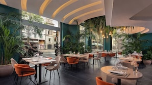 Un restaurante moderno con mesas en el interior, ventanas amplias y plantas de interior.