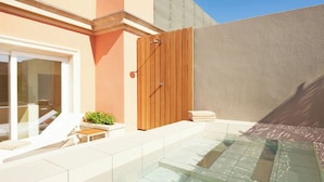 Un área de piscina moderna al aire libre con valla de madera, puerta de cristal y una pequeña zona de estar con mesa y sillas.