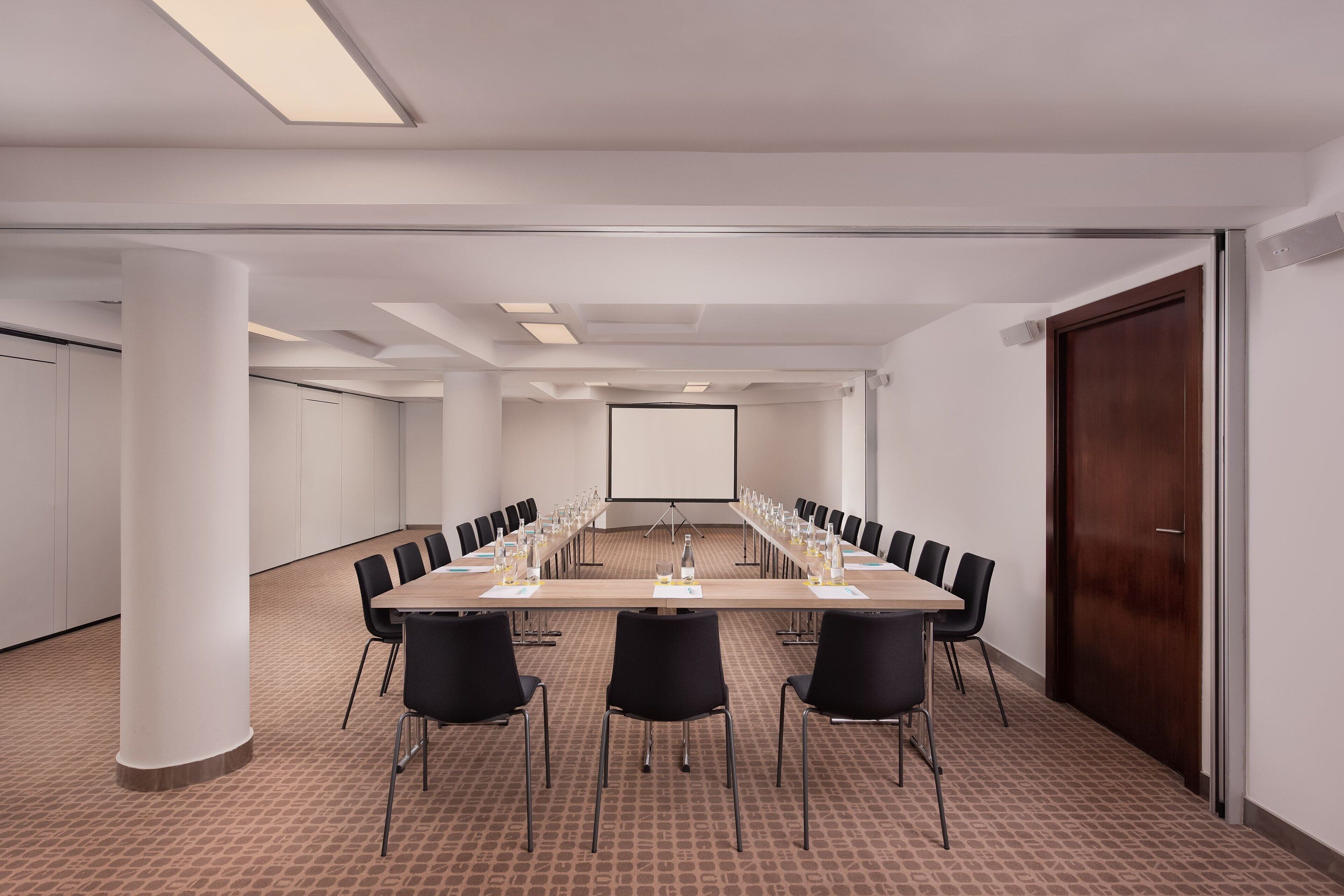 Una sala de conferències amb una taula llarga, cadiretes negres i una pantalla projectora.