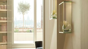 Un pasillo moderno con una puerta de cristal que da a un balcón, una silla negra y un estante con un jarrón.