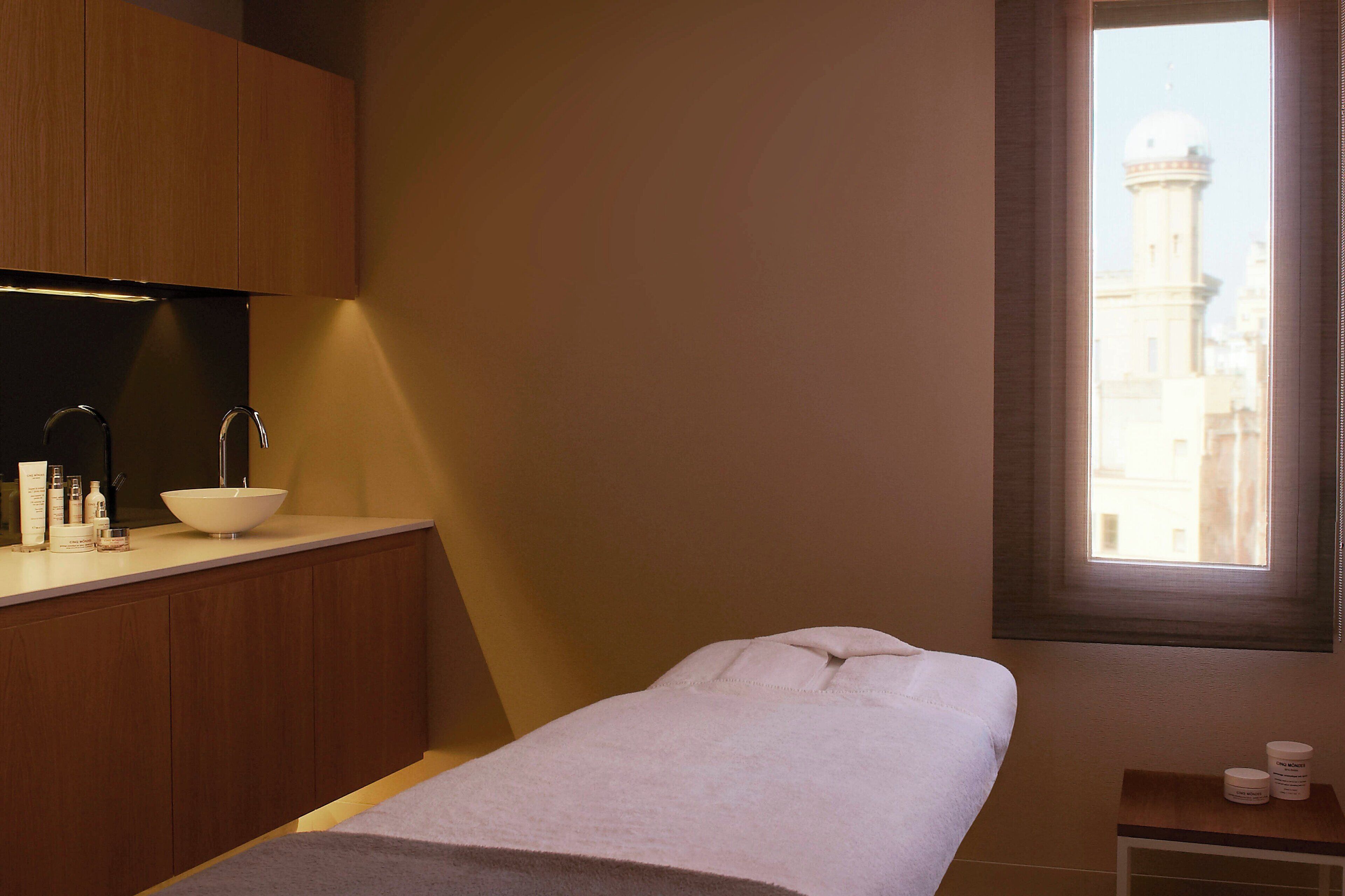 A hotel room with a wooden vanity, a white sink, and a bed with a white towel.