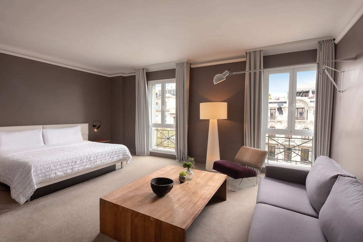 A hotel room with a bed, a sofa, a coffee table, a chair, and a lamp.