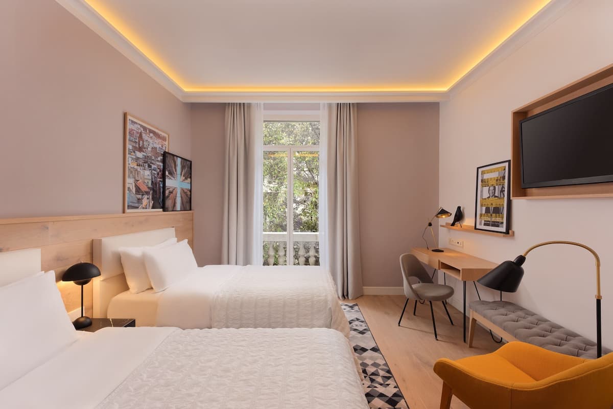 A hotel room with two beds, a desk with a chair, a TV, and a window with curtains.
