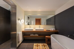 A modern bathroom with two sinks, a large mirror, a bathtub, and a shower area. - Le Meridien Barcelona (Barcelona)