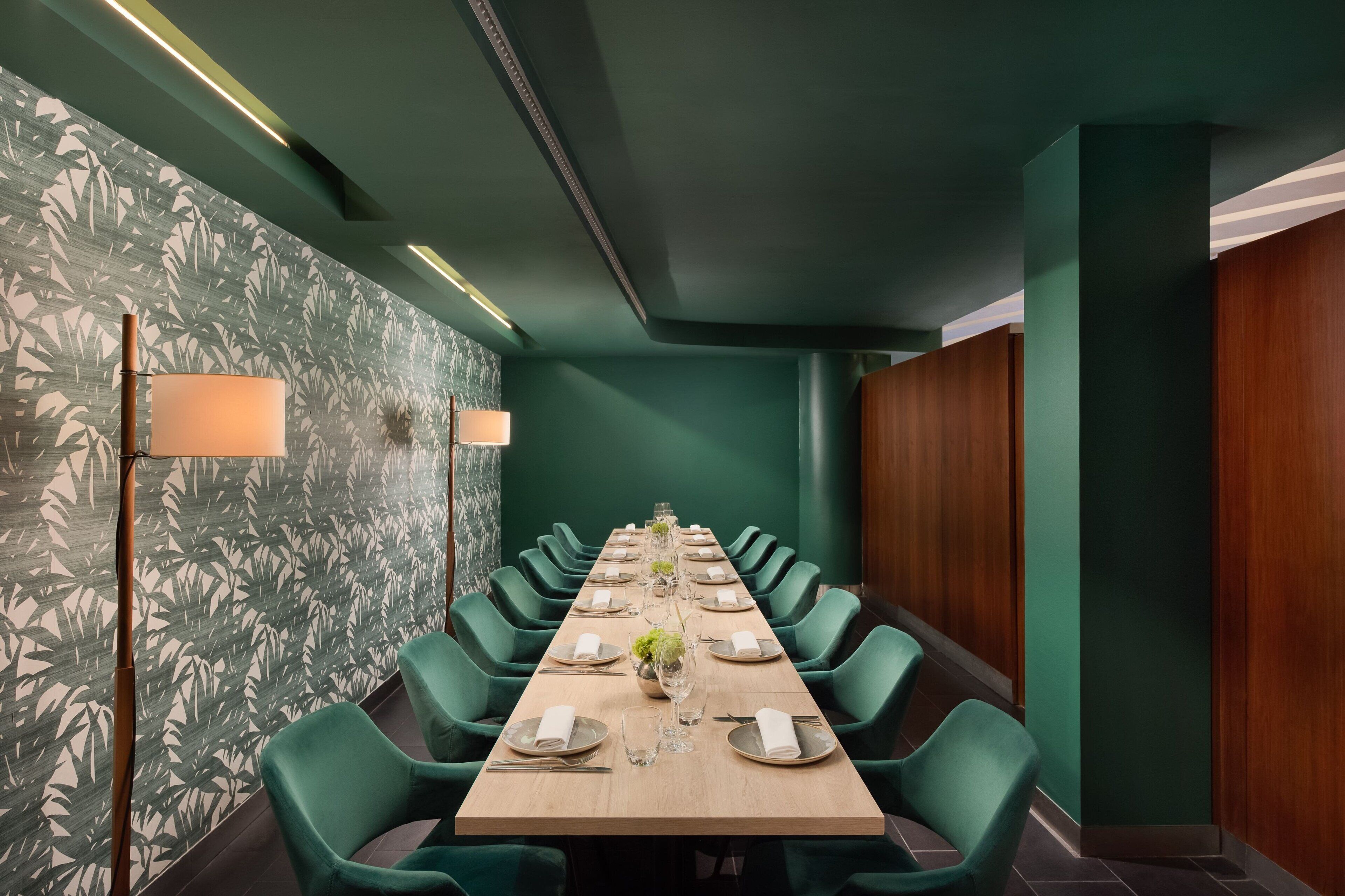 A conference room with a long table set for a meeting, surrounded by green chairs, and a patterned wallpaper on the walls.