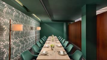A conference room with a long table set for a meeting, surrounded by green chairs, and a patterned wallpaper on the walls.