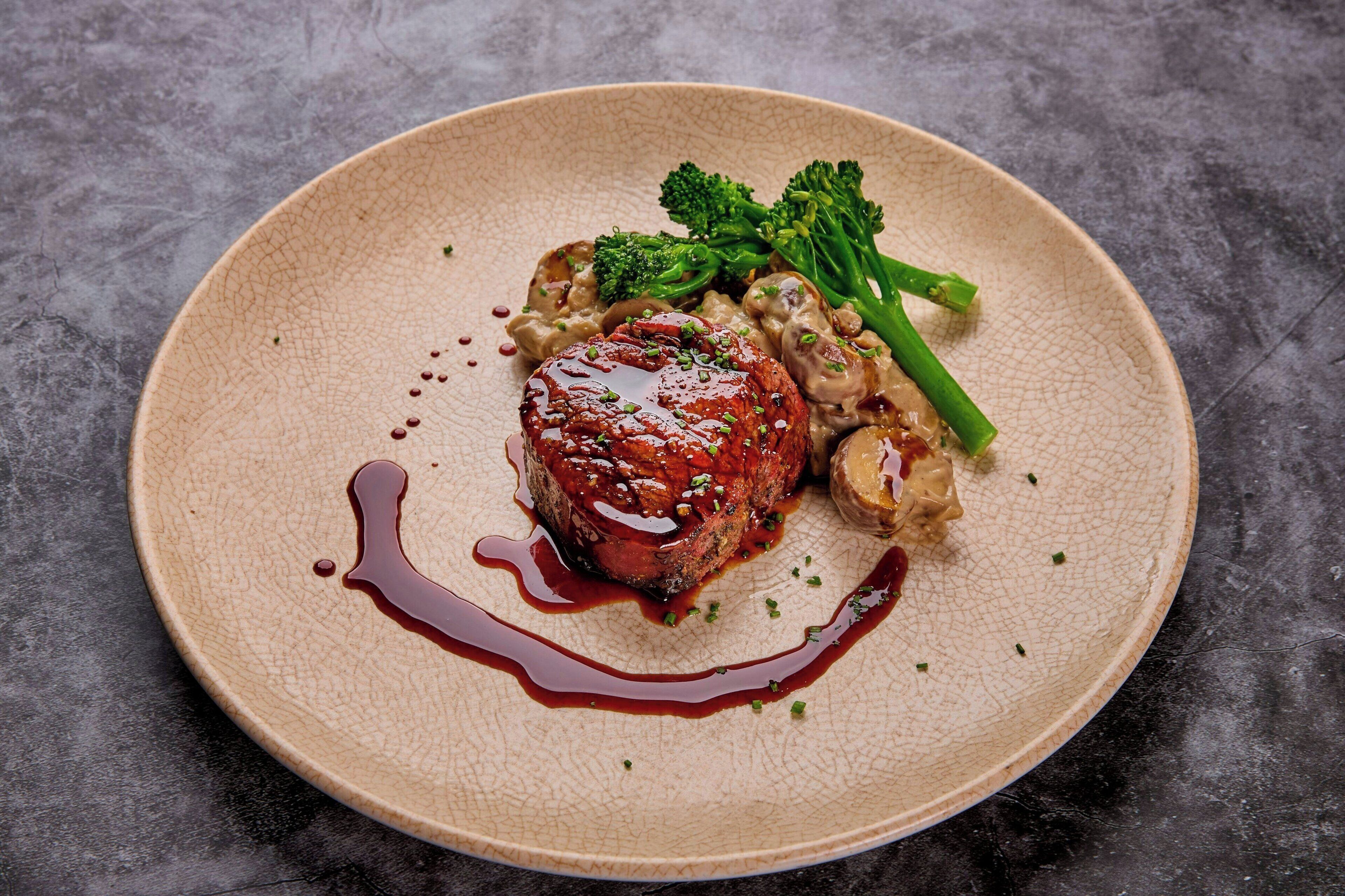 Un plato con bistec, champiñones y brócoli sobre una fuente texturizada.