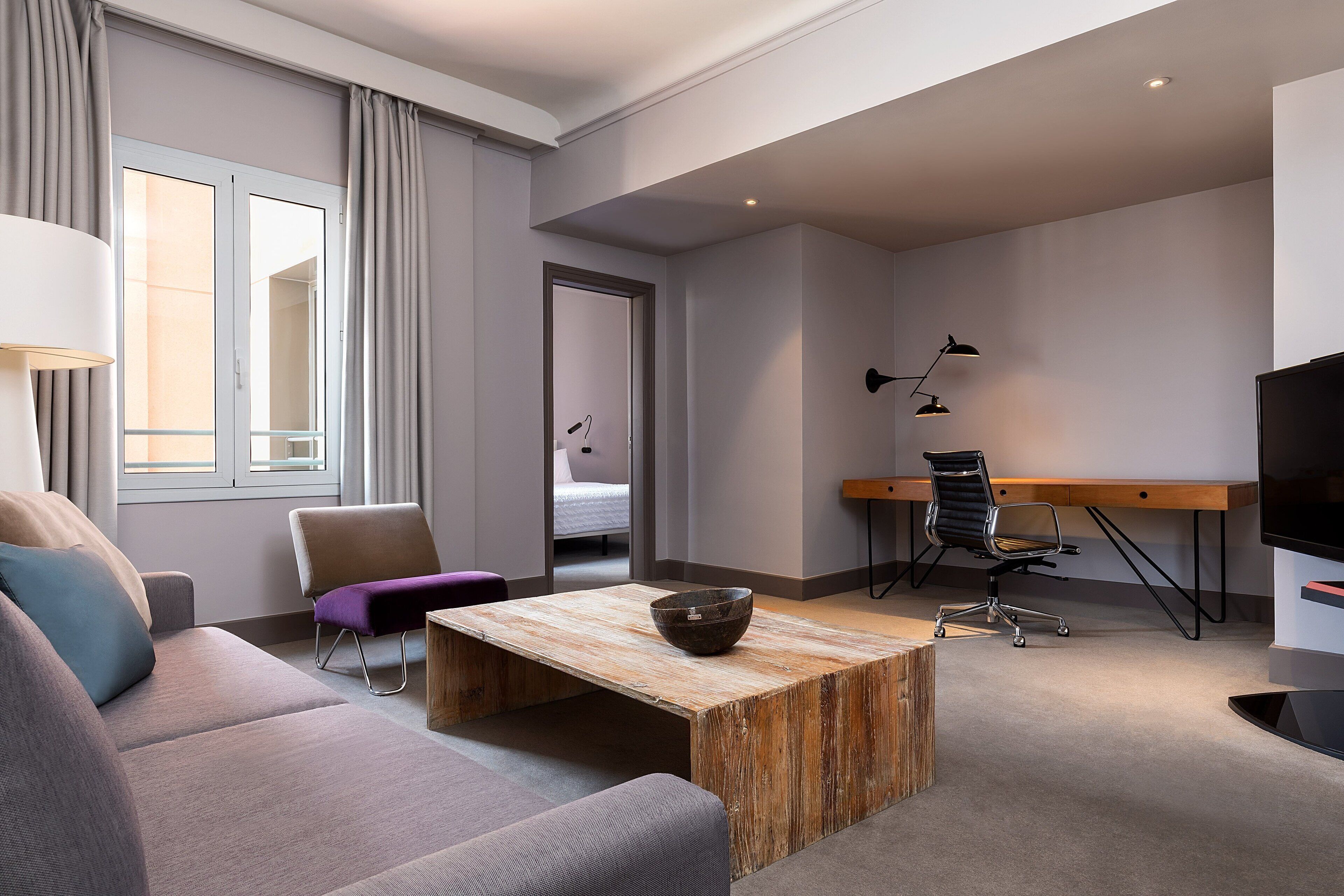 Una habitación de hotel moderna con un sofá, una mesa de centro de madera, un escritorio y un televisor.