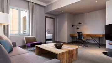 Una habitación de hotel moderna con un sofá, una mesa de centro de madera, un escritorio y un televisor.