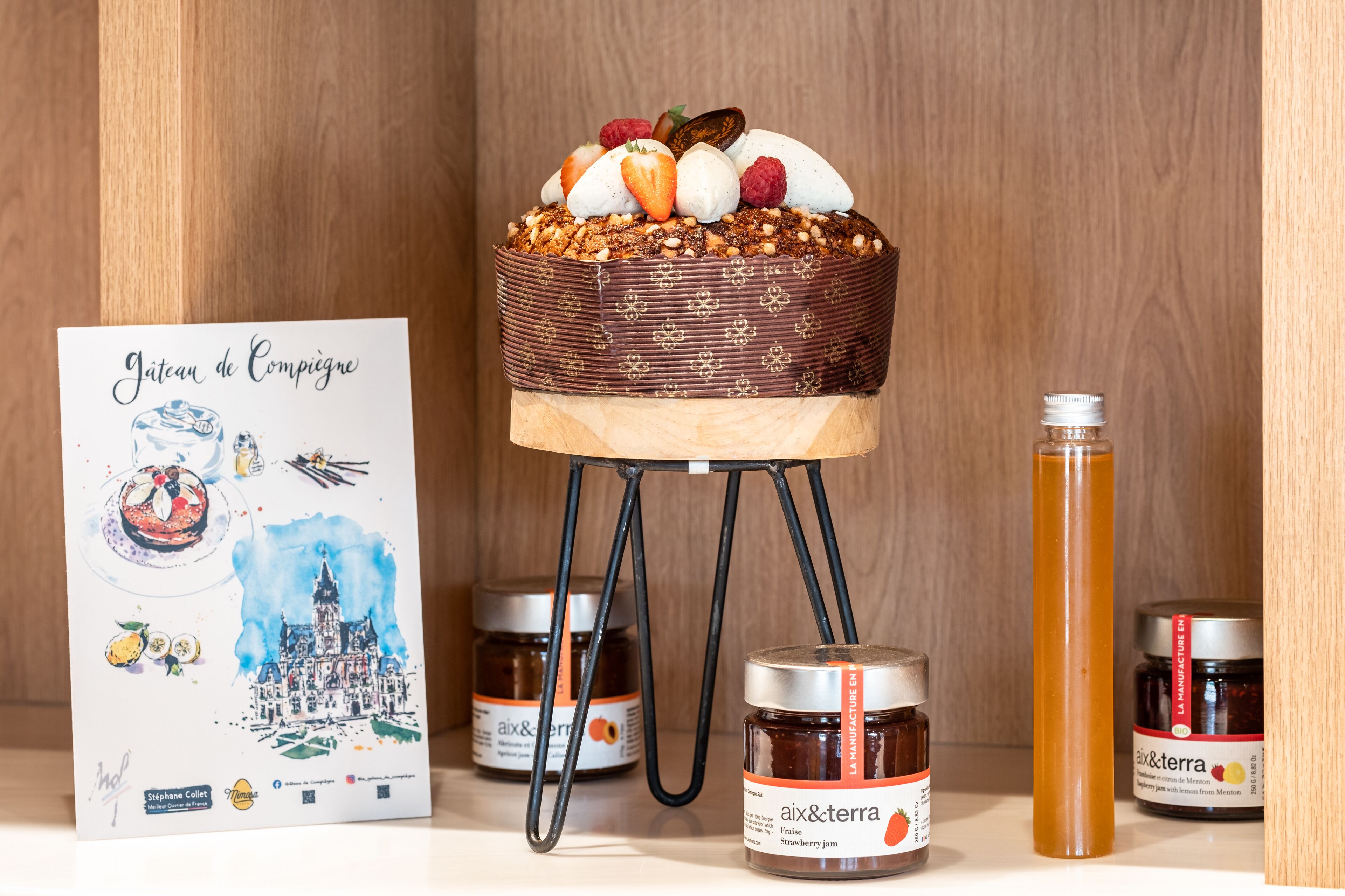 A cake on a stand with a sign depicting a castle and jars of jam.