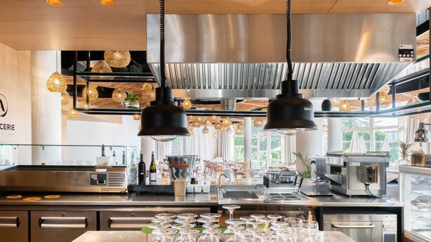 A modern kitchen with stainless steel appliances, hanging pendant lights, and a central island with wine glasses. - Mercure Compiegne Sud (Lacroix-Saint-Ouen)