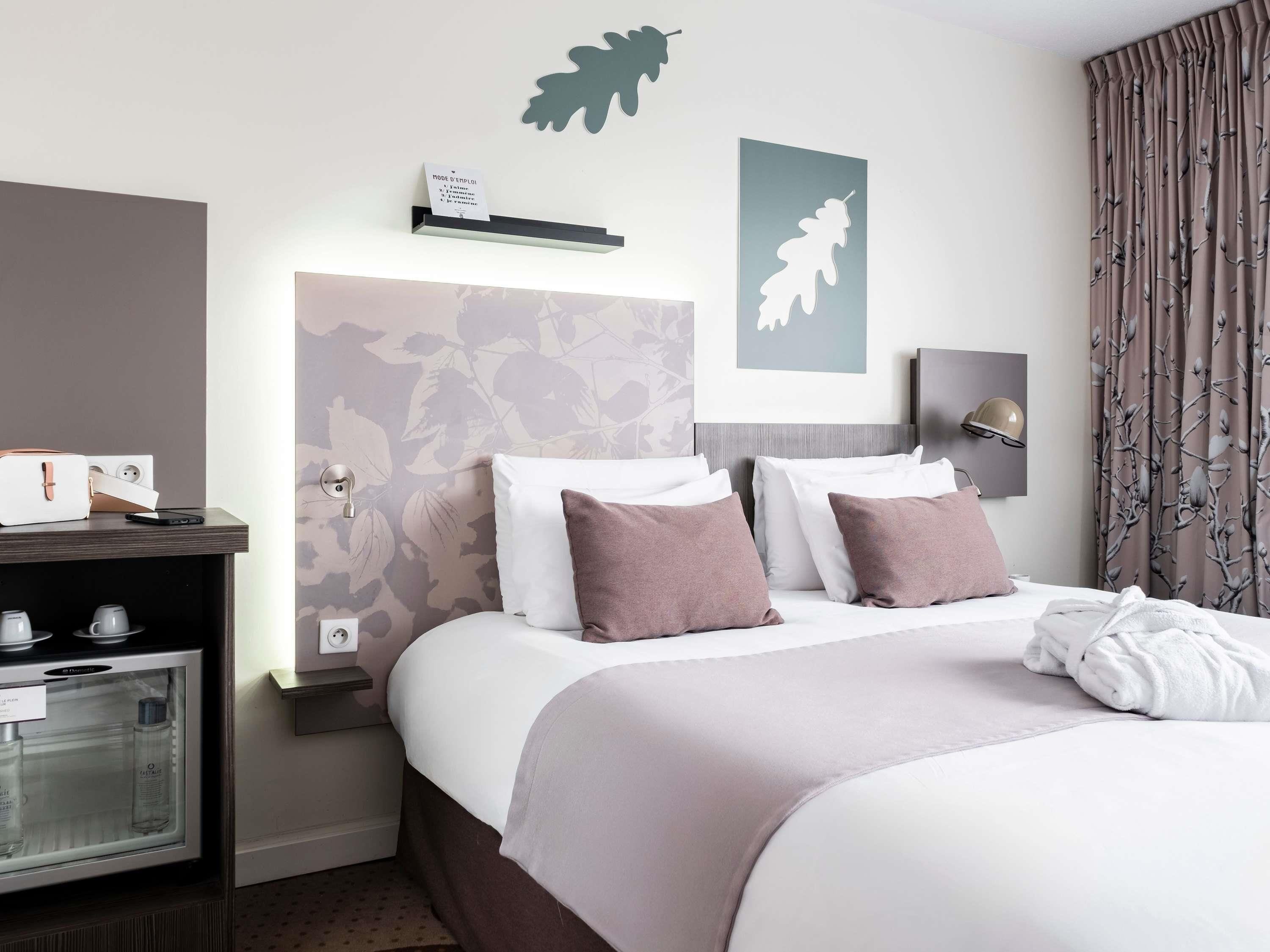 A hotel room with a bed, a nightstand, a minibar, and a wall-mounted shelf.
