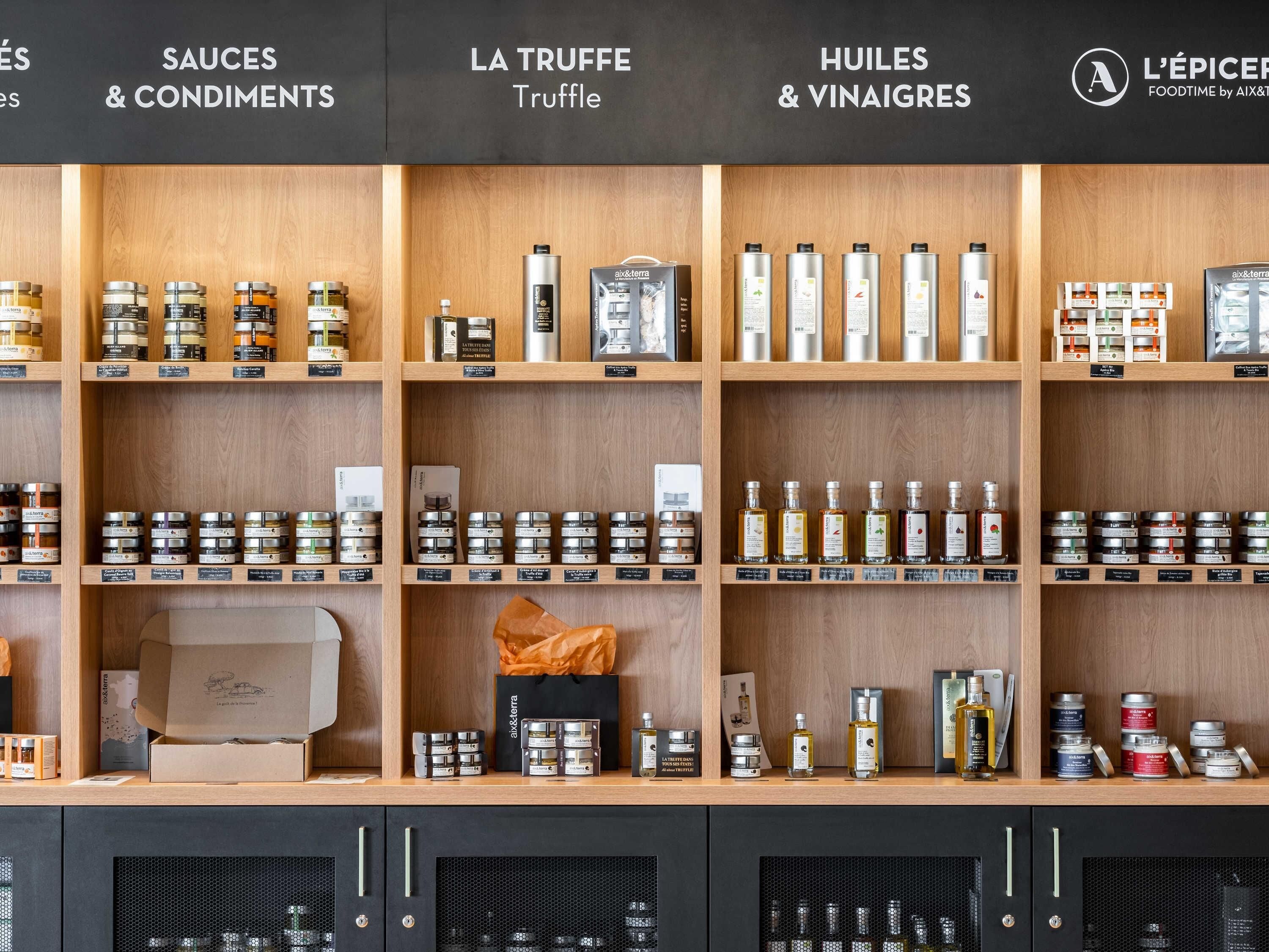 A store with shelves labeled 'SAUCES & CONDIMENTS,' 'LA TRUFFLE Truffle,' and 'HUILES & VINAIGRES.'