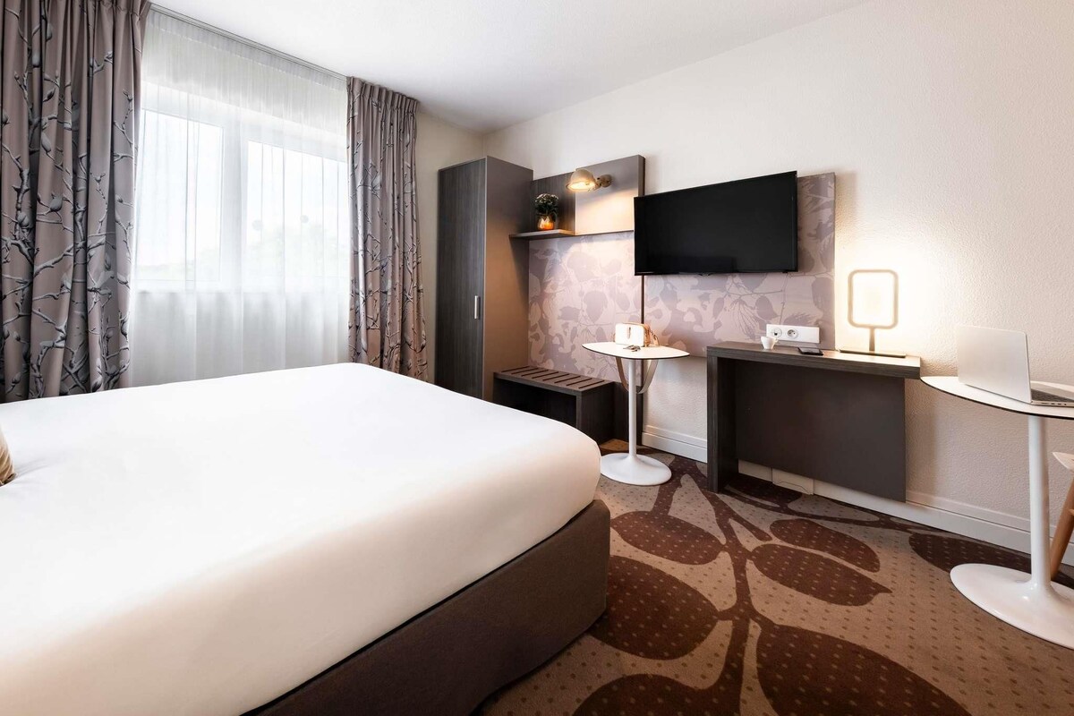 A hotel room with a bed, a desk, a TV, and a lamp.