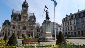 A historic building with a statue, a flag, and a well-maintained garden with a bench. - Mercure Compiegne Sud (Lacroix-Saint-Ouen)