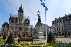 A historic building with a statue, a flag, and a well-maintained garden with a bench. - Mercure Compiegne Sud (Lacroix-Saint-Ouen)